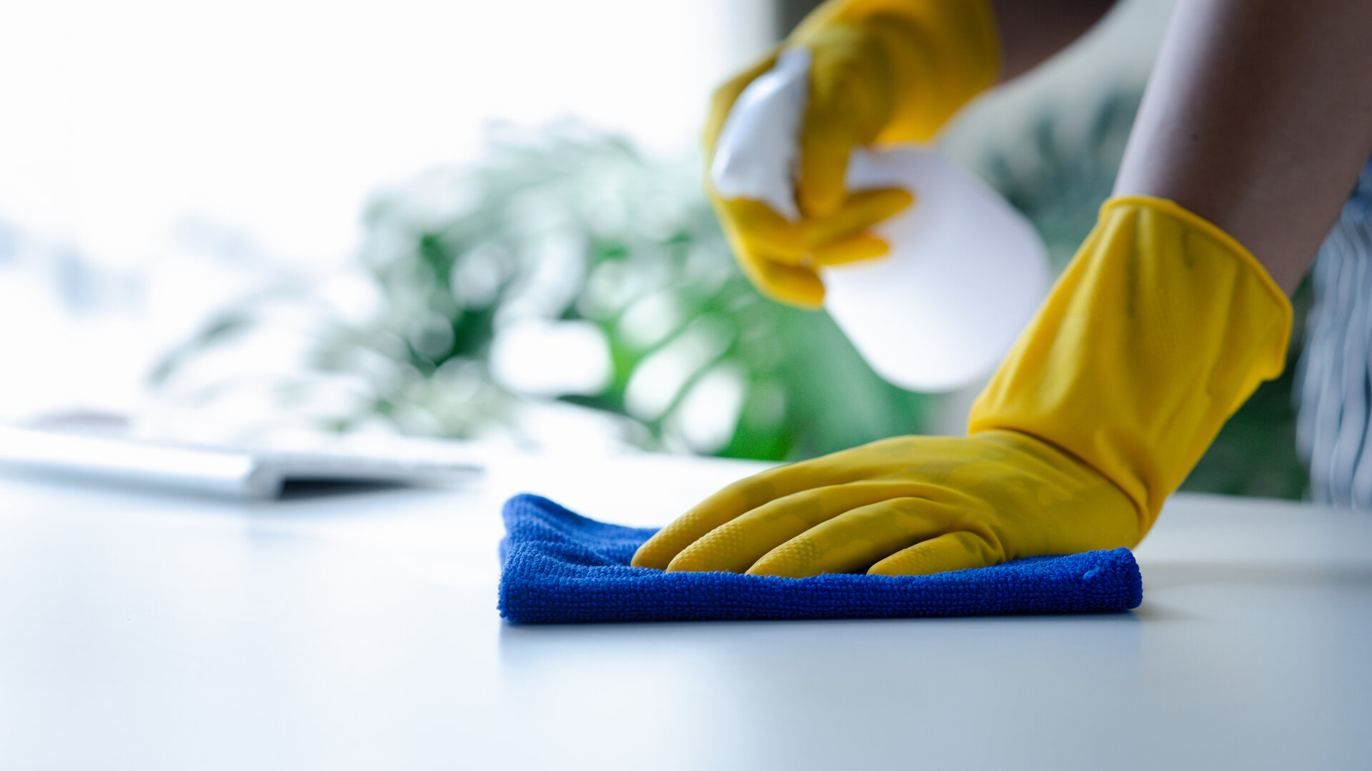 Reinigung mit gelben Handschuhen und blauer Mikrofaser auf weißer Oberfläche